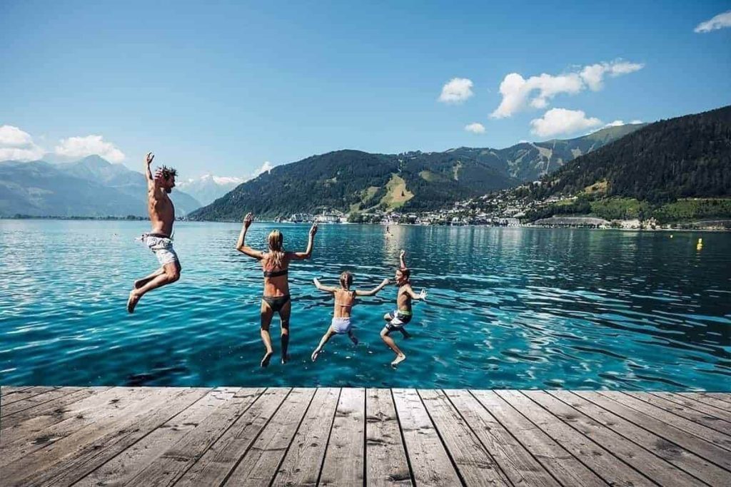 Family jumping into the water of Lake Zell in Kaprun, surrounded by mountains and nature.