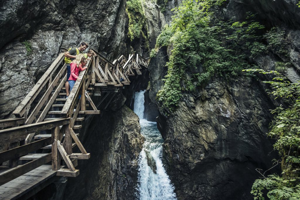 Familie steht auf Holzbrücke über einen Wasserfall in der Natur bei Kaprun.